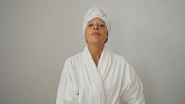 Bornoz ve havlu giymiş bir kadın, izole edilmiş beyaz arkaplan üzerinde kendine güvenen bir ifadeyle italyan jesti yapıyor. Parmakları duygu gösteren orta yaşlı bir güzellik.