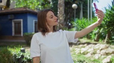 Güzel genç bir kadın arka planda mavi bir ev olan şehir parkında selfie çekiyor..