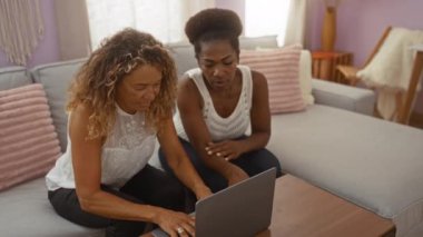 Kadınlar rahat bir oturma odasında dizüstü bilgisayarda birlikte çalışıyorlar, ekranda bir şey tartışıyorlar, kapalı bir çalışma ortamı sergiliyorlar..