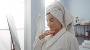 Esmer saçlı genç bir kadın sağlık merkezinde spa tedavisi görüyor. Kafasında beyaz bir bornoz ve havlu var..