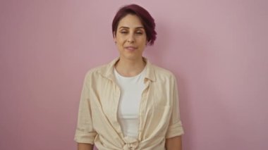 Kadın, genç, kendine güvenen, beyaz bir güzel gömlek giyiyor, dişleriyle ayakta duruyor ve gülümsüyor, mutlu ve pozitif görünüyor izole pembe bir arka planda.