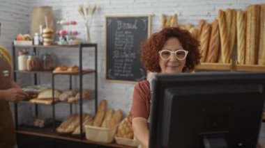 İki fırıncı, bir erkek ve bir kadın, yeni pişmiş ekmek ve hamur işleriyle çevrili iyi organize edilmiş bir fırında birlikte çalışıyorlar.