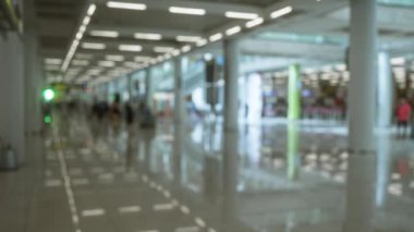 Yolcularla dolu bir havaalanı terminalinin bulanık görüntüsü, sönmüş ışıklar ve parlak zemindeki yansımalar, seyahat ortamını ve dinamik hareketi vurguluyor