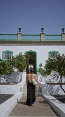 Güneşli bir açık havada büyüleyici beyaz bir otel terasına doğru yürüyen bir kadın.