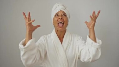 Bornoz ve havlu giymiş, kızgın orta yaşlı bir kadın kollarıyla bağırıyor ve bağırıyor. İzole edilmiş beyaz arka plan çılgın ifadesi ve stresli duygular yüzünden hayal kırıklığına uğruyor. 
