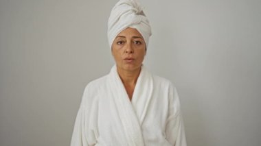 Havlu ve bornoz giyen kadın, tamam parmaklarından bakıyor, şaşırmış yüz ifadesi, soyutlanmış beyaz arka plan, orta yaşlı esmer, neşeli ve mutlu duygu gösteren kadın.