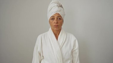 Bornoz ve havlu giymiş, üzgün bir ifade takınan, beyaz arka planda soyutlanmış orta yaşlı, ağlayan, stresli ve endişeli bir kadın. 
