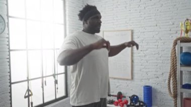 Genç bir Afrikalı Amerikalı spor salonunda spor yapıyor. Etrafı ekipman ve beyaz tahtayla çevrili. Formda ve azimli..