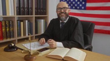 Amerikan bayrağı, kitapları, pulları ve masasında tokmağı olan yargıç cüppeli bir adam..