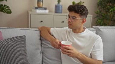 Genç İspanyol bir adam modern bir oturma odasında oturuyor, elinde pembe bir bardak, ve uzaktan gülümsüyor..