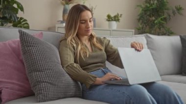 Güzel genç bir kadın evdeki rahat bir koltukta otururken dizüstü bilgisayar kullanıyor. Etrafı şehir ortamında rahat yastıklarla çevrili..