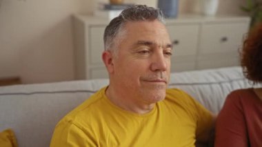 Orta yaşlı çift evdeki rahat bir oturma odasında kanepede otururken birbirlerine sevgiyle sarılıyorlar.