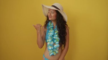 Yaz şapkalı genç Çinli kadın Hawaii zambağı ile gülümsüyor ve sarı arka planı işaret ediyor.
