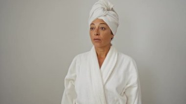 Bornoz ve havlu giymiş bir kadın, orta yaşlı ama enerjik, şaşırmış bir ifadeyle, ağzı açık, ilerideki bir şeye şaşırmış, izole edilmiş beyaz bir arka plan.