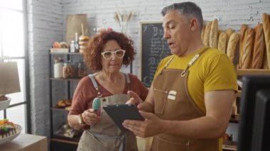 Erkek ve kadın fırında fırıncılar, arka planda ekmek somunları sergilenen kapalı dükkanda bir tablet tutarak bir tartışmaya giriştiler.