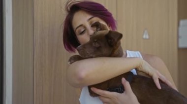 Mor saçlı genç bir kadın evcil köpeğini ahşap bir duvarın önünde şehir sokaklarında kucaklıyor..