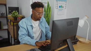 Genç Afrikalı Amerikalı bir adam, kitaplarla ve bitkilerle çevrili bir ofis çalışma alanında bilgisayarının başında bir başarı ve üretkenlik duygusu taşıyarak coşkuyla kutlama yapıyor..