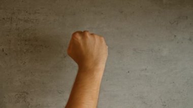 Duvarın arkasında el hareketlerini gösteren bir adam var. Kapalı yumruk ve uzatılmış orta parmak da dahil.