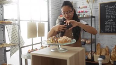 Çin 'deki bir fırında çalışan genç bir kadın, akıllı telefonunu bir dükkanın içinde çeşitli fırınlanmış ürünlerle sergilenen hamur işlerinin fotoğrafını çekmek için kullanır..
