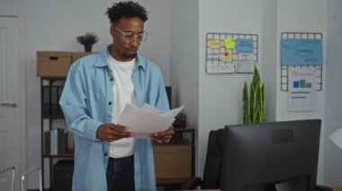 Genç, yakışıklı, sakallı, Afro-Amerikan bir adam bir ofiste çalışıyor, elinde kağıtlar, ve kapalı bir işyerine odaklanmış görünüyor..