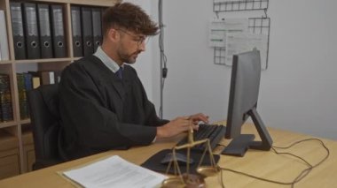 Yargıç cübbesi giyen genç adam ofiste bilgisayar başında çalışıyor. Masasında adalet terazisi ve belgeler var. Hukuk kitaplarıyla çevrili.