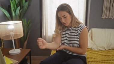 Yatak odasında bir yatakta oturan genç bir kadın endişeli bir ifadeyle kolunu muayene ediyor..