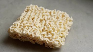 Gri yüzeyde duran pişmemiş hazır ramen eriştesi bloğu.