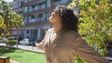 Genç, güzel bir İspanyol kadın, arka planda ağaçlar ve binalar olan bir şehir parkında gün ışığının tadını çıkarıyor..