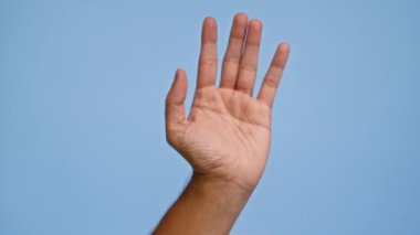 Renkli bir fotoğrafta mavi arka planı olan kapalı bir eli gösteren bir adam video çerçevesinde bir jest sergiliyor.