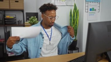 Ofiste odaklanmış, sakallı ve gözlüklü sıradan giyinmiş, evrak işlerine dalmış, kapalı bir iş yerinde yakalanmış bir Afrikalı Amerikalı..