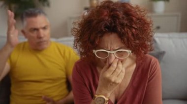 Kadın, erkekler oturma odasında tartışırken evde ilişki gerilimi ve duygusal gerilimi gösteriyor.