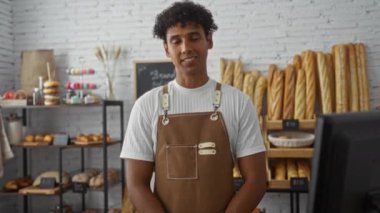 Genç adam fırında dikilmiş, çeşitli ekmek ve hamur işleri ile çevrili, önlük giymiş, kapalı alanda, gülümseyen, erkek, dükkan, İspanyol, yetişkin, yakışıklı,