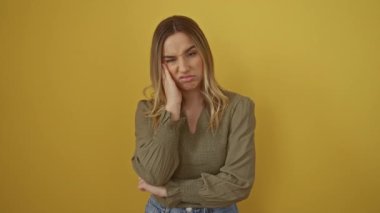 Sarı arka planda duran genç sarışın kadın yorgun görünüyor, sıkılmış ve çapraz kollarla düşünüyor depresyon ve duygusal problemlerle mücadele ediyor.