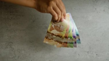 Beton bir yüzey üzerinde el ele tutuşan Kanada doları, farklı değerlerde canlı banknotlar sergiliyor.