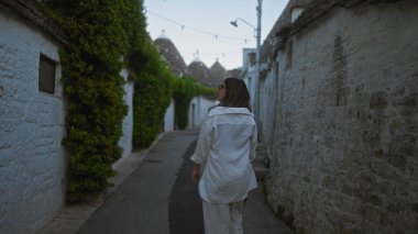Genç bir İspanyol kadın Alberobello caddesinde yürüyor, İtalya 'nın Puglia şehrindeki geleneksel Trulli evlerine hayran kalıyor..