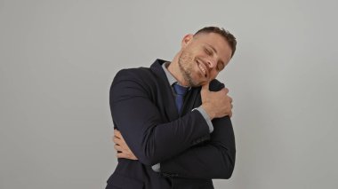 Yakışıklı bir adam beyaz bir arkaplana karşı takım elbisenin içinde mutlu bir gülümsemeyle kendine sarılıyor.
