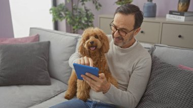 İspanyol adam ve kaniş modern oturma odasındaki kanepede tablet kullanıyorlar..