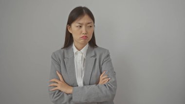 Gri takım elbiseli, kollarını çapraz bağlamış, hoşnutsuz genç bir Çinli kadın beyaz bir arka plana karşı duruyor..