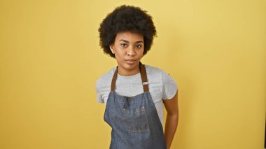 Kıvırcık saçlı Afrikalı bir Amerikalı kadın sarı bir arka plana karşı önlük giymiş, güzelliği ve güveni somutlaştırıyor..