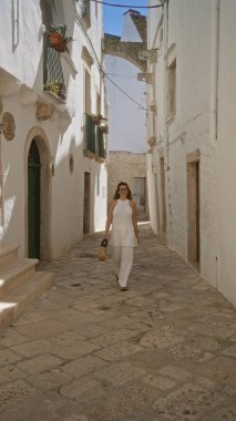Güzel, genç bir İspanyol kadın beyaz binalar ve Avrupa mimarisi ile çevrili Locorotondo, Puglia, İtalya 'nın büyüleyici eski sokaklarında yürüyor..