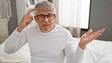 Gözlüklü yaşlı adam yatak odasında el kol hareketi yapıyor.