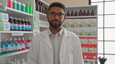 Kendine güvenen bir erkek eczacı, ilaç raflarıyla çevrili modern bir eczanede duruyor..