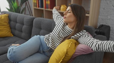 Rahat ve genç bir İspanyol kadın rahat bir oturma odasındaki kanepede uzanmaktan zevk alır..