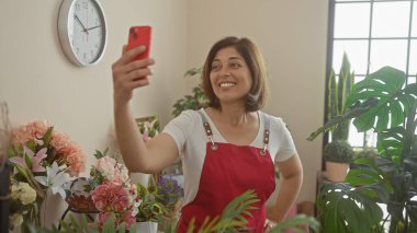 İspanyol kadın çiçekli bir çiçekçide çiçeklerle çevrili bir önlükle selfie çekiyor..