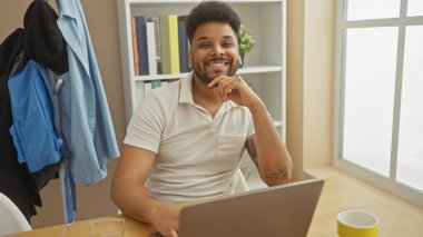 Evde bilgisayarda çalışan gülümseyen sakallı bir adam. Masasında kahve ve gözlüklerle.