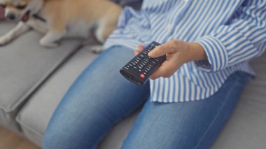 Orta yaşlı bir kadın evdeki kanepede köpeğiyle uzaktan kumandayı tutuyor.