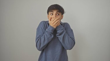 Genç bir adam beyaz bir arka planda ağzını kapatan şaşkın bir ifadeyle