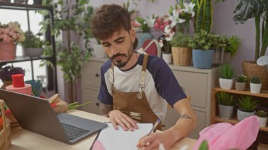 Çiçekçide notlar alan yakışıklı İspanyol bir adam. Etrafı bitki ve buketlerle çevrili..