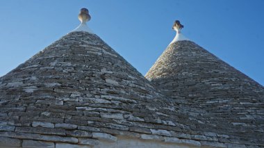 Alberobello 'da, Puglia' da, İtalya 'da, açık mavi gökyüzü altında, konik çatıları olan tarihi taş trulli evler geleneksel mimariyi ve bu Avrupa şehrinin büyüleyici manzarasını gözler önüne seriyor..