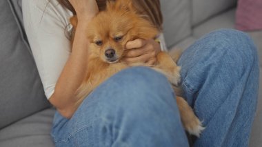 Genç bir kadın, evinde sıcak ve sevgi dolu bir an için kanepede Pomeranian köpeğine sarılıyor.